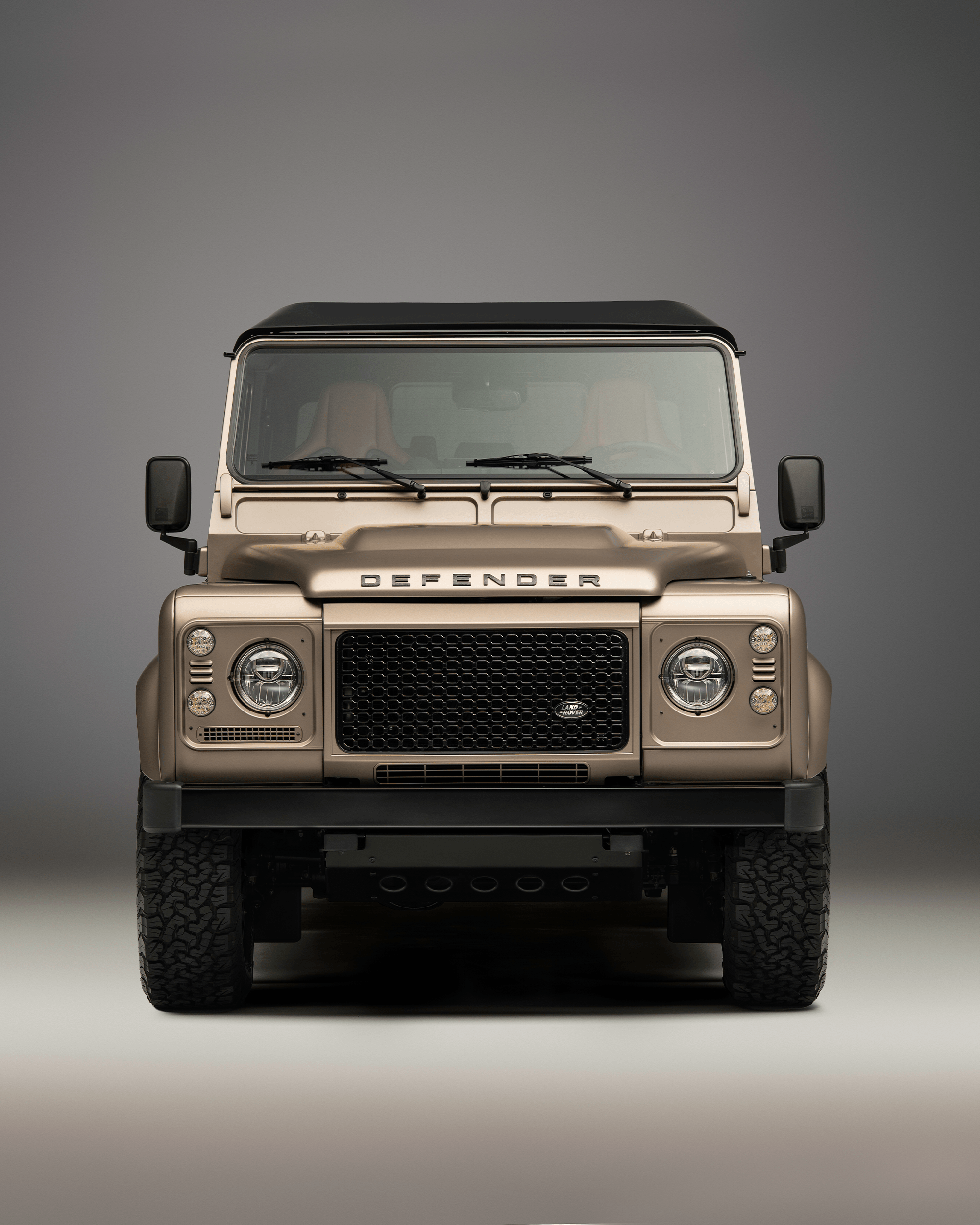 Front view of a Defender parked on a sandy path with dunes and the sea in the background.