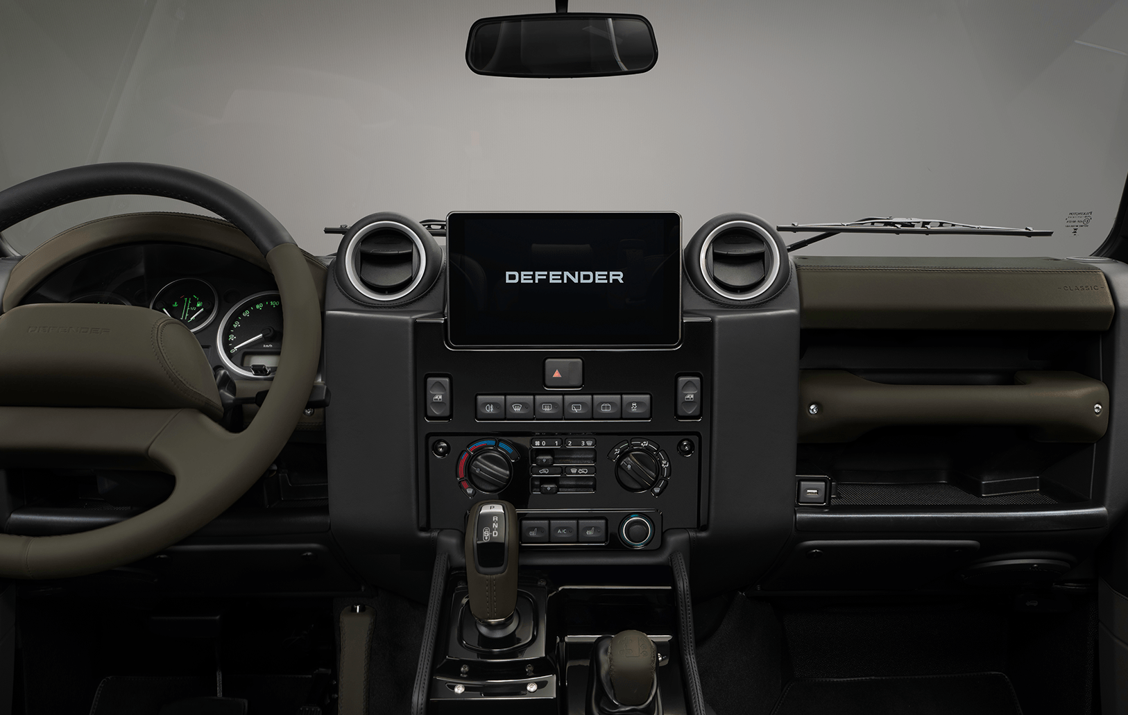 Rear view of a Classic Defender parked on a sandy beach with the ocean in the background.