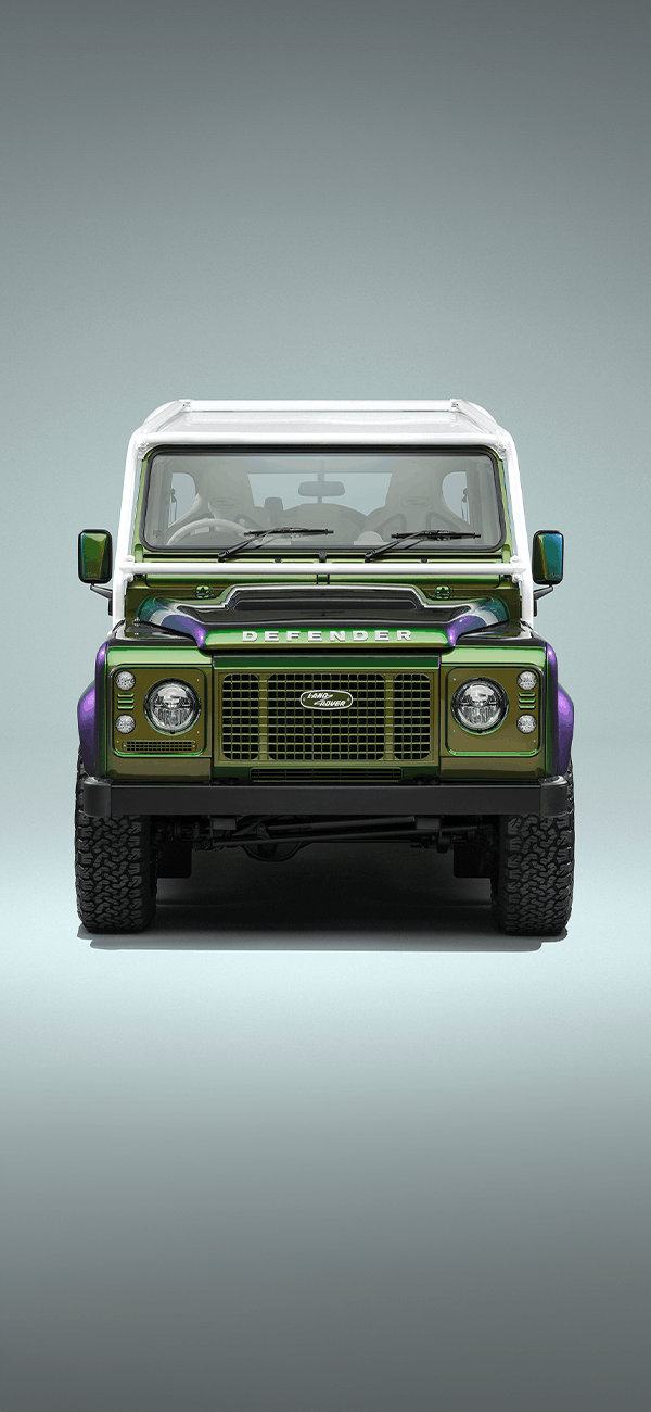 A red Defender V8 in the sand and grass.